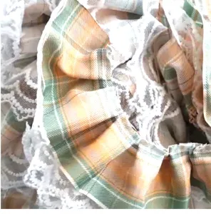 Macro detail view of the ruffled white lace trim on the plaid fabric of a pet collar