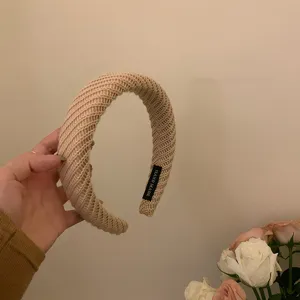 Detailopname van de brede beige gebreide haarbandtextuur met zachte stof en handgemaakt label.