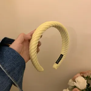 Gedetailleerd overzicht van een stijlvolle gele brede gebreide haarband met handgemaakt label.