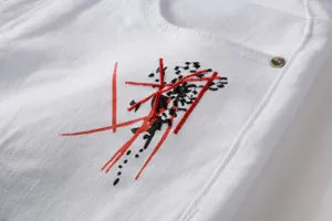 Close-up detail of white slim-fit denim jeans featuring unique black and red artistic embroidery.