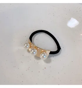 Detailopname van een zwart haarelastiek met gouden metalen plaat en drie kunstparels.