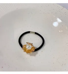 Detailopname van een zwart haarelastiek met gouden schelphanger en witte parel.