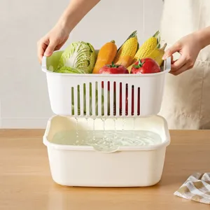 Funktionaler weißer doppelstöckiger Küchen-Abtropfkorb mit frischem Gemüse und Wasser.