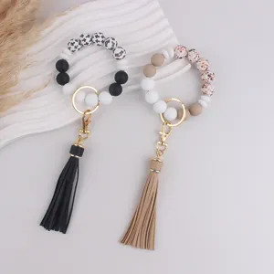 Detailed view of silicone beaded keychain bracelet with tassel on white textured background.