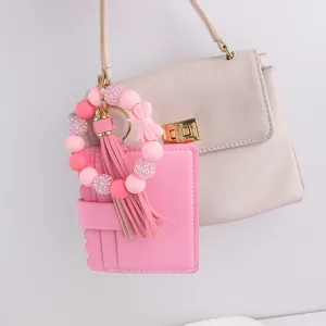 Cartera tarjetero de pulsera con cuentas de silicona rosa, lazo y detalle de borla.