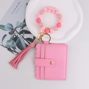 Cartera rosa con tarjetero, pulsera de cuentas de silicona y llavero con lazo y borla.