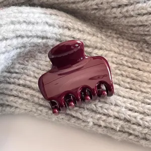 Nahaufnahme eines weinroten glänzenden Harz-Haarklammer-Details, minimalistisches Accessoire.