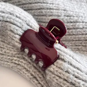 Nahaufnahme einer glänzenden dunkelroten Haarklammer mit welligem Rand an grauem Strickstoff.