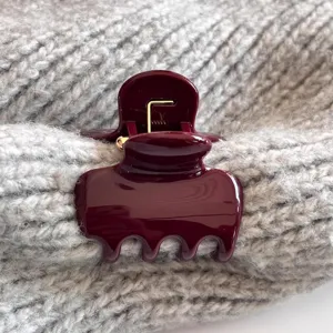 Bequeme burgunderrote Haarklammer im Detail, glänzender Mini-Clip auf grauem Strickstoff.