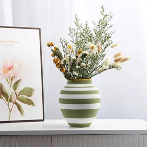 Close-up of green and white striped ceramic vase with dried flowers in a home setting.