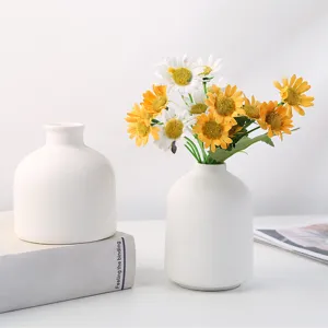 Gros plan de vases en céramique blanche avec des marguerites sur un bureau chic
