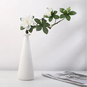 Détail d'un vase en céramique blanche minimaliste avec des fleurs artificielles sur bureau