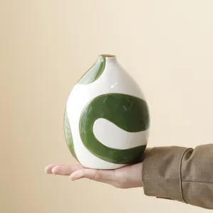 Macro detail of a hand-painted ceramic vase with green swirls held to show scale