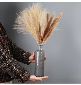 Dettaglio di un vaso rustico in ceramica grigia con erba pampas essiccata tra le mani