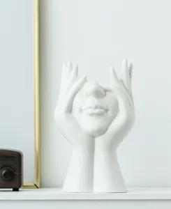 Vue détaillée d'un vase en céramique blanc brillant en forme de mains tenant un visage d'art.