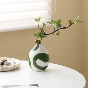 Close-up of a hand-painted green swirl ceramic vase on a white minimalist table