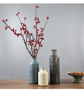 Disposizione dettagliata di tre vasi in ceramica rustica con un ramo di bacche rosse.