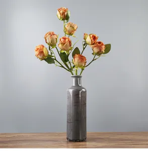 Vaso rustico in ceramica craquelé con rose arancioni artificiali sul tavolo.