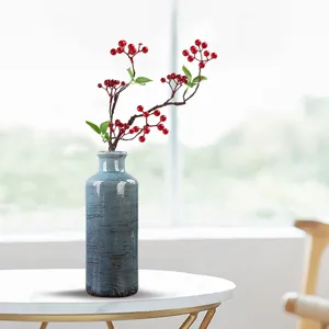Vaso rustico in ceramica blu ghiaccio con rami di bacche rosse su tavolo di marmo