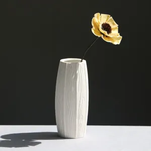 Modern white ceramic vase with wood grain texture and a single yellow dried flower.