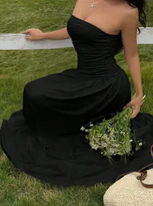 Detail view of a black strapless maxi dress with ruched waist in a sunny outdoor field