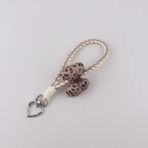 Cute leopard print bow braided phone strap detail showcasing keychain and heart clasp.