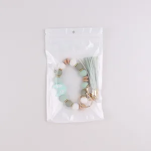 Detalle de llavero pulsera de cuentas de silicona con colgante de luna y borla en bolsa transparente.