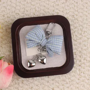 Blue checkered fabric bow keychain with dual metal heart pendants and clasp accessory.