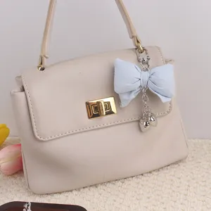 Close-up detail of the elegant beige handbag featuring a light blue fabric bow pendant.