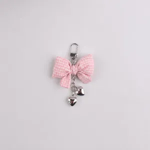 Close-up detail of pink gingham fabric bow keychain with cute silver heart charms and metal clasp.