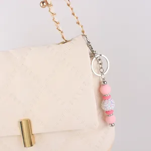 Close-up detail shot of a stylish beige quilted bag featuring a cute pink beaded keychain charm.