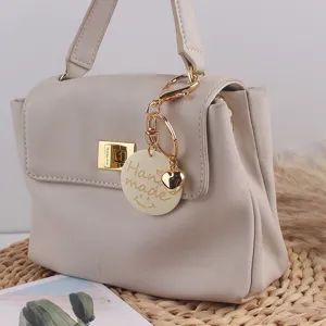 Detailansicht der hellgrauen Handtasche mit Goldschloss und handgemachtem Schlüsselanhänger.