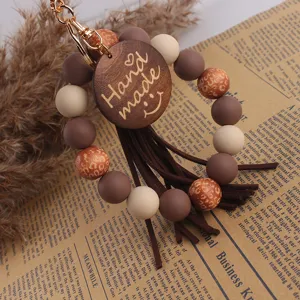 Détail de porte-clés perles en silicone, pendentif en bois souriant et pompon cuir.