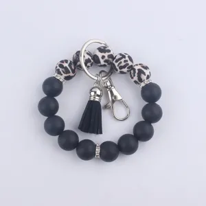 Détail de porte-clés bracelet en perles de silicone avec perles imprimé léopard et gland noir.