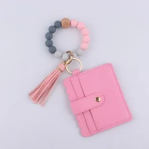Detalle llavero cuentas silicona, tarjetero PU rosa, accesorio pulsera borla vista cercana.