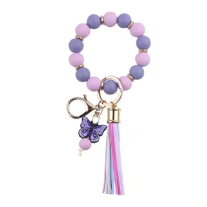 Detailed shot of silicone beaded wrist keychain with purple butterfly charm and rainbow tassel.
