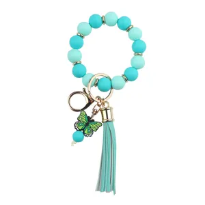 Close up view of turquoise silicone bead wristlet keychain with green butterfly charm and tassel.