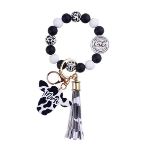 Close-up of cow print silicone bead keychain with tassel and Mama pendant on white background