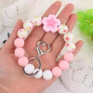 Silicone bead wristlet keychain detail, pink floral pendant and heart clasp closeup shot.