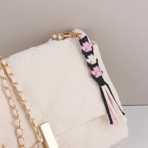 White quilted shoulder bag detail with handmade woven flower strap and gold chain accent.