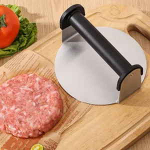 Close-up of a stainless steel burger press with a black handle on a wooden cutting board.