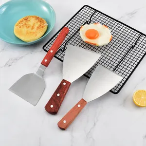 Dettaglio di tre raschietti per pasta in acciaio inox con manici in legno su marmo