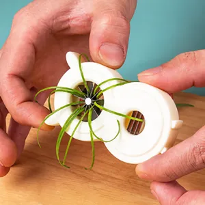 Detailed view of a white plastic scallion shredder tool slicing green onions on wood board