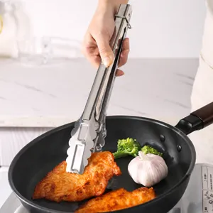 Pince de cuisine en acier inoxydable retournant du poulet grillé dans une poêle