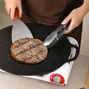 Stainless steel spatula and tongs set with black griddle pan for home cooking burgers and steaks safely.