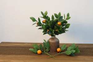 Primo piano dettaglio di rami di arancio artificiali e vaso con fogliame per arredo.