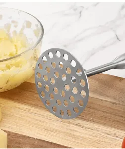Gros plan détaillé d'un presse-purée en acier inoxydable avec plaque perforée sur planche.