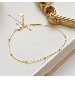Close-up detail of a minimalist gold snake bone anklet with round beads on a vintage book.