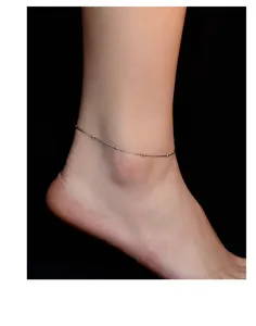 Close-up detail of a delicate silver snake bone anklet with small sparkling beads on ankle.