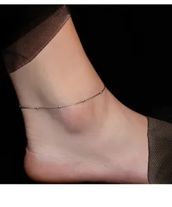 Close-up detail of sterling silver snake chain anklet with delicate beads on ankle.